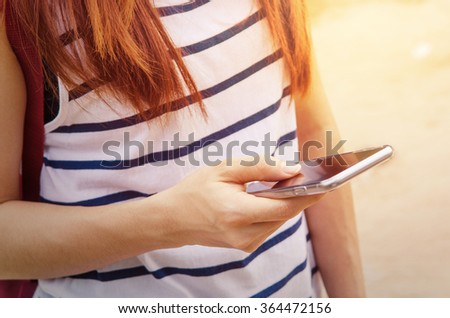 woman holding and using smart phone while standing outdoors at sunny evening