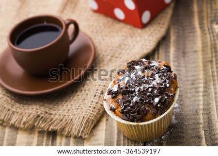Beautiful tasty muffin with chocolate on top near brown cup of strong fragrant coffee standing on sackcloth napkin appetizing refreshment break time closeup on wooden background, horizontal picture