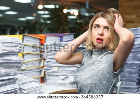 Office businesswoman at her desk full of documents, showing an overwhelmed expression