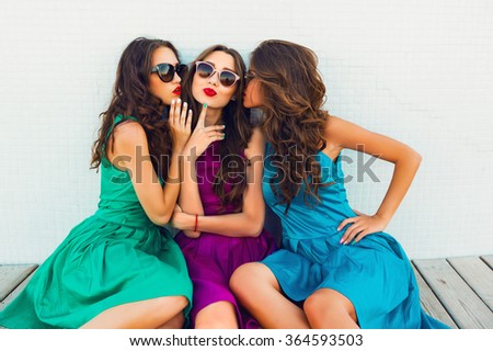 Three young pretty sisters having fun  outdoor. Wearing elegant color dress, have wavy hairs, stylish sunglasses. 