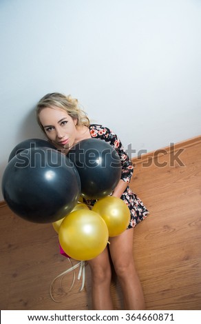 Beautiful model sitting on wooden floor leaning back against white wall peeking head out from black and golden balloons