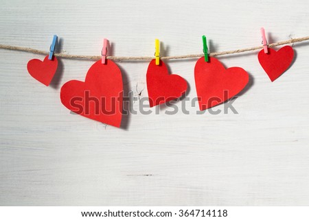 Red bright paper hearts hanging on rope on a white wooden background