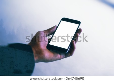 Smartphone holding in hipster hand with blank screen on blue background