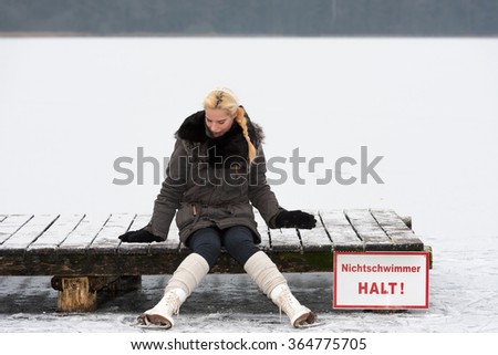 Young woman takes a break while skating and sitting on a jetty. German inscription on the shield: Non-Swimmer Stop! 