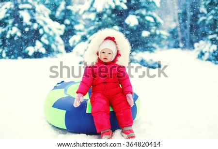 Little child sitting on sled in winter snowy day