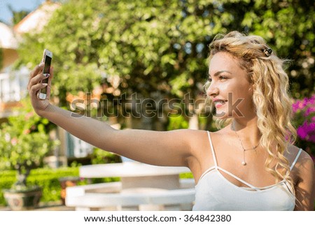 Portrait of a beautiful young woman selfie in the park with a smartphone