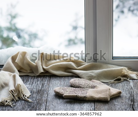 Beige woolen scarf and mittens located on stylized wooden window sill. Winter concept of comfort and relaxation. Royalty-Free Stock Photo #364857962