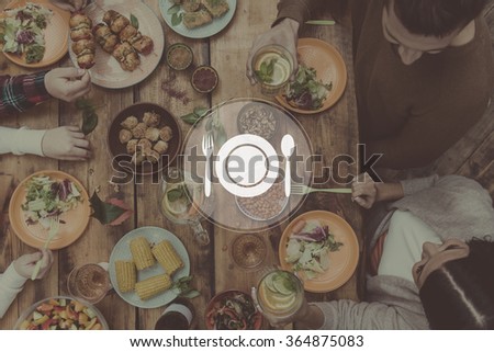 Getting together for dinner. Digitally composed picture of kitchen utensil over top view of four people having dinner together while sitting at the rustic wooden table