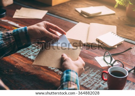 Unexpected letter. Close-up image of man opening an envelope while sitting at the rustic wooden table  Royalty-Free Stock Photo #364882028