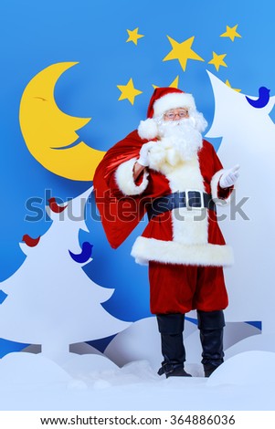 Santa Claus standing with his bag of giftsin a cartoon fairy snowy forest. Full length portrait.