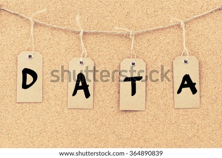 Vintage grunge tags with letters on rope string, word DATA over cork board texture background, filter applied, available copy space. 