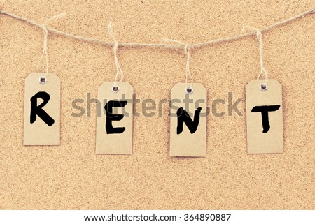 Vintage grunge tags with letters on rope string, word RENT over cork board texture background, filter applied, available copy space. 