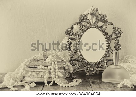 Antique blank victorian style frame, perfume bottle and white pearls on wooden table. black and white style photo. template, ready to put photography 