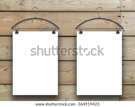 Close-up of two hanged paper sheets with clothes hangers on horizontal brown wooden boards background