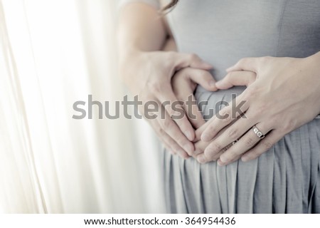 Beautiful Young Pregnant Woman and Her Husband Together Caressing Her Pregnant with fingers Heart symbol .selctive focus at ring