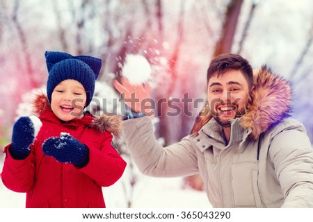 active father and son playing snowballs in winter park