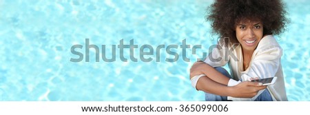 panoramic image of young Black woman during spring break using her phone near pool.