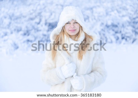 Beautiful happy smiling young woman in white fur coat on winter park nature background