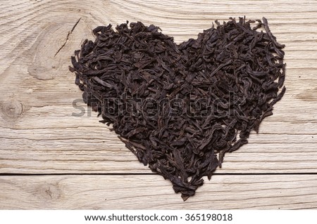 Dried black tea in the form of heart on wooden background, top view