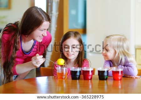 Young mother and her two little daughters painting colorful Easter eggs at home