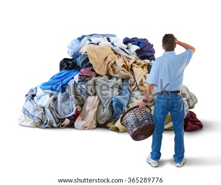 A distraught man with his hand to his head and a laundry basket in his hand is standing in front of a giant pile of dirty clothes overwhelmed by this household chore Royalty-Free Stock Photo #365289776