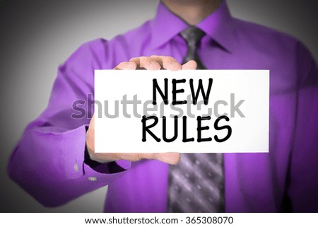 Businessman in blue shirt and gray tie shows a card with the inscription new rules. Man on a gray background. Selective focus.