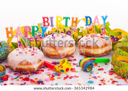 three doughnuts with with frosting, confetti and streamer - birthday decoration with candles on white background - candles with text "happy birthday"
