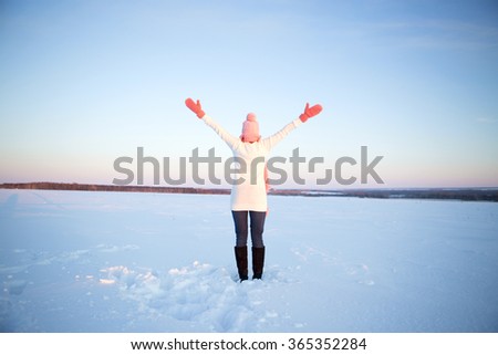Beautiful healthy young woman breathing fresh air with her arms raised and outstretched up while in the snowed mountains during a winter snow day, outdoors.