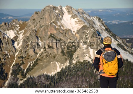 Tourist with rucksack in front of rocky mountains during winter trip in nature