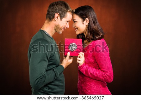 Cheerful couple holding gift box against shades of brown