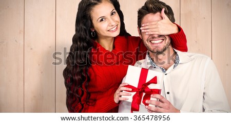 Young woman covering eyes of partner holding gift against wooden planks