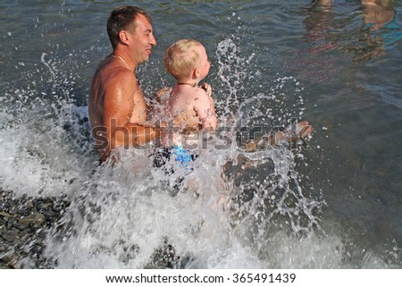 Photo father and son swimming in the waves of the sea. Water splashes.