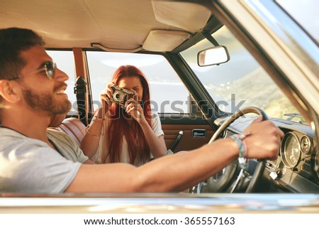 Young couple on a road trip. man driving car with woman taking pictures with retro camera.