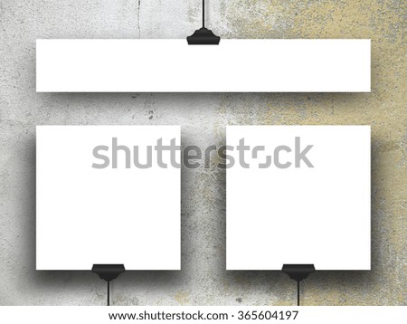 Close-up of three hanged square and rectangular paper sheets with clips on grey and beige weathered wall background