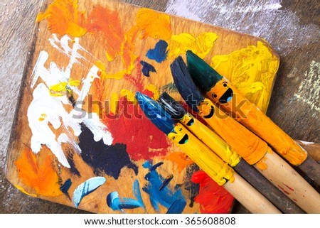 Colored brushes smile fun and happy, round and his hair colored in blue and emerald. Brushes are close to the palette