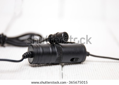 Close view of a tiny lavalier type microphone on a white wooden background.