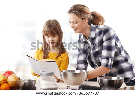 Portrait of cute girl holding in her hand a recipe book while cooking together with her mom.
