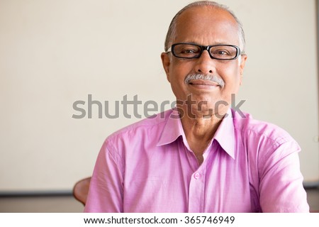 Closeup portrait, smart elderly man in pink shirt with dark eye glasses, specs, sitting down, isolated indoors white chalkboard background Royalty-Free Stock Photo #365746949