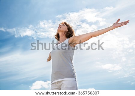 breathing outside - zen middle aged yoga woman opening up her chakra with arms raised,practicing meditation for freedom over summer blue sky,low angle view Royalty-Free Stock Photo #365750807