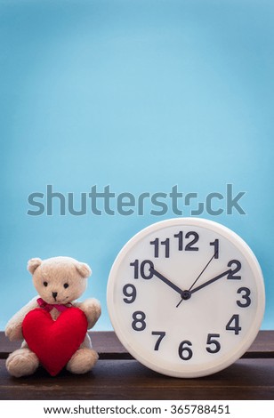 Teddy bear with pink heart and clock decoration on wooden table over wall blue background, Valentine day concept