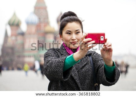 Young beautiful woman tourist taking pictures on mobile phone on the background Red Square, Moscow Kremlin, Russia