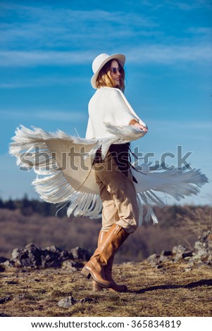 Happy country woman enjoying nature in mountains wearing poncho, hat and sunglasses