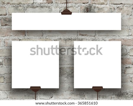 Close-up of three hanged square and rectangular paper sheets with clips on grey weathered brick wall background