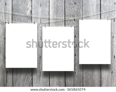 Close-up of three hanged paper sheets with pegs on monochrome wooden boards background