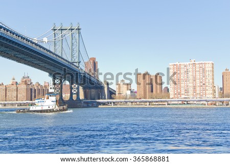 Boat passing below Manhattan Bridge on winter morning with manhattan buildings in background.