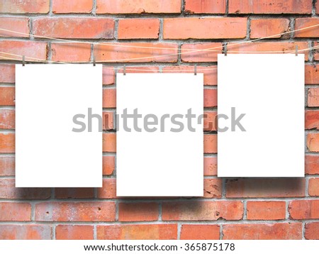 Close-up of three hanged paper sheets with pegs on red brick wall background