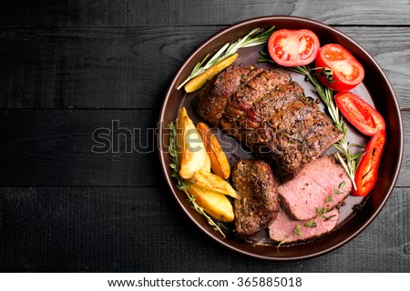 Grilled beef on a cutting board with potatoes and vegetables Royalty-Free Stock Photo #365885018