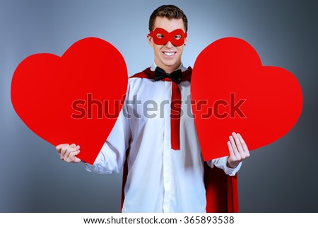 Young handsome man in a superhero costume holding a red hearts. Love concept. Valentine's Day.