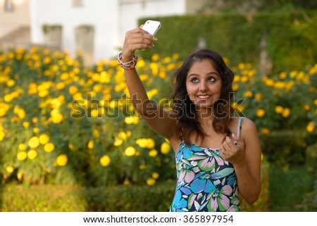 Indian woman outdoors in park using mobile phone to take selfie picture