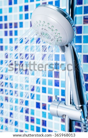 Shower head with running water against blue tiled bathroom wall